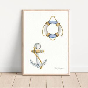 Puede incluir: Una pintura de acuarela de un salvavidas azul y blanco y un ancla plateada con una cuerda dorada. La pintura está sobre un fondo blanco con una firma en la esquina inferior derecha.