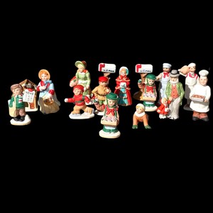 May include: A collection of 15 miniature figurines depicting various Christmas characters. The figurines are made of porcelain and feature detailed painted designs. The characters include a baker, a mail carrier, a child with a newspaper, and a child with a pig.