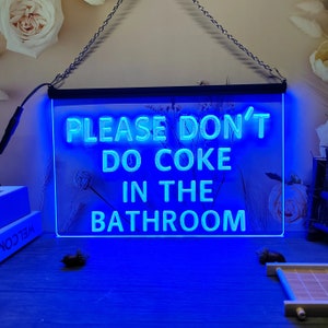 May include: Blue neon sign with the text "Please don't do coke in the bathroom".