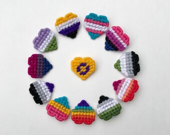 May include: A circle of 12 small crocheted hearts in various colors and patterns, including a yellow heart with a purple circle in the center. The hearts are arranged in a circle around the yellow heart.