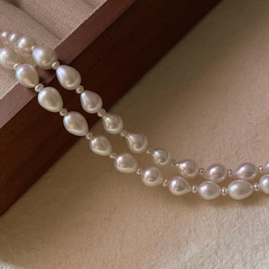 May include: A double strand of white pearl necklace with a teardrop shape. The pearls are strung on a thin silver chain.