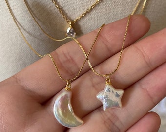 May include: Two gold chain necklaces with pearl pendants. One pendant is a crescent moon shape and the other is a star shape.