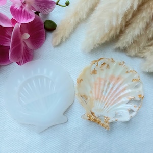 May include: A white seashell resin tray with gold leaf accents. The tray is next to a silicone mould of the same seashell.