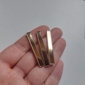 Może przedstawiać: Trzy prostokątne płytki lustrzane w kolorze złotym.