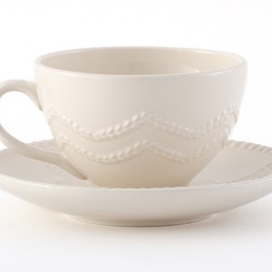 Puede incluir: Un juego de taza y platillo de té de cerámica blanca con un delicado diseño en relieve de tallos de trigo entrelazados. La taza tiene una forma redondeada y un asa.