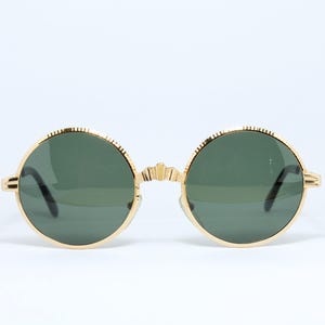 Peut inclure: Lunettes de soleil rondes avec une monture dorée et des verres vert foncé.