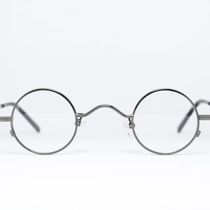 May include: A pair of round, silver-toned eyeglasses with thin metal frames.