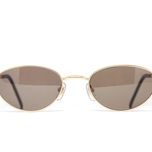 May include: Gold-tone oval-shaped sunglasses with brown lenses.