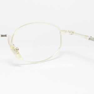 May include: Close-up of a pair of silver-rimmed eyeglasses with clear lenses. The glasses have a classic round shape and are set against a white background. The frames are thin and delicate.