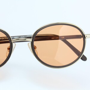 May include: Round sunglasses with a gold frame and brown temples. The lenses are a light orange color. The text "YOHJI YAMAMOTO" is visible on the frame.