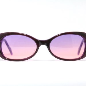 Könnte beinhalten: Lilafarbene, ovale Sonnenbrille mit einem pink-violetten Verlaufsglas.