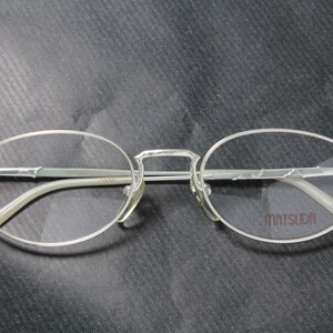 May include: Silver-toned eyeglasses with oval lenses and a bridge. The temples and frame are thin and metallic. The brand name "MATSUDA" is printed on the right lens.