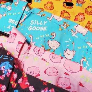 May include: Four different fabric patterns for shirts. The top shirt is yellow with a cartoon character. The second shirt is blue with a white goose and the text "Silly Goose" and "he he he". The third shirt is pink with a cartoon character. The bottom shirt is black with a blue and red cartoon character and the text "ソニック" and "ピイ".