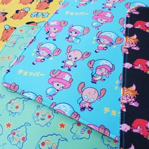 May include: Three different mousepads with colorful cartoon designs. The first mousepad is yellow with a cartoon dog design. The second mousepad is blue with a cartoon character design and the text "チョッパー". The third mousepad is black with a cartoon character design.