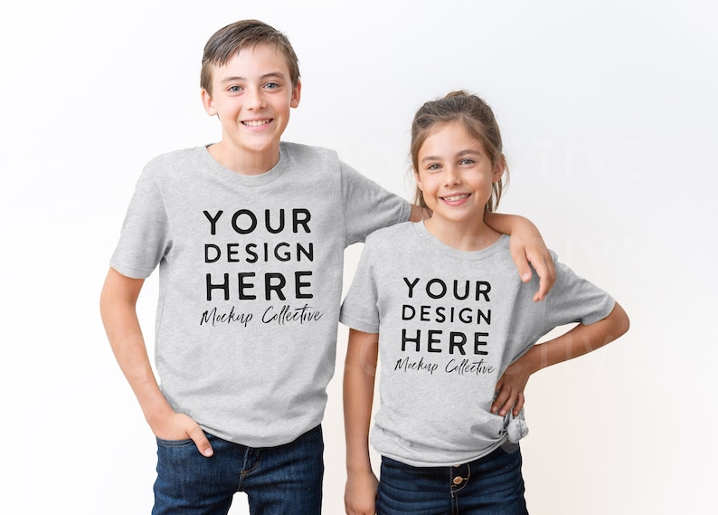 May include: Two children wearing grey t-shirts with the text "YOUR DESIGN HERE Mockup Collective" printed on the front. The children are standing side-by-side, with the boy on the left and the girl on the right. They are both smiling and looking at the camera.