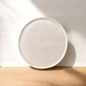 Può includere: Un piatto da portata in ceramica bianca con una superficie leggermente strutturata. Il piatto ha la parola "cure" incisa sulla superficie.