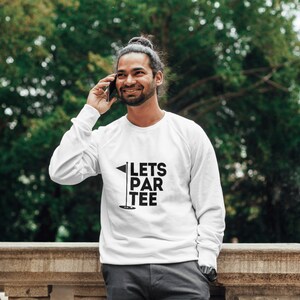 Puede incluir: Sudadera blanca de manga larga con texto negro que dice "Lets Par Tee" y un gr&aacute;fico de bandera de golf negro.