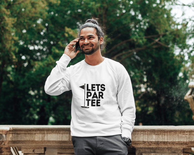 Puede incluir: Sudadera blanca de manga larga con texto negro que dice "Lets Par Tee" y un gr&aacute;fico de bandera de golf negro.