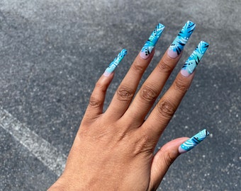 Peut inclure: Gros plan sur une main avec de longs ongles de forme carrée, peints en bleu clair et blanc avec un motif.