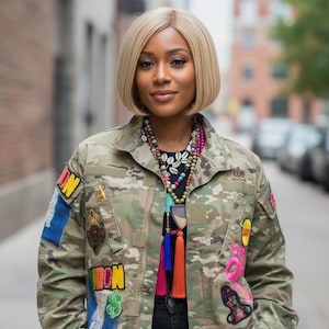 May include: A woman wearing a camouflage jacket adorned with colorful patches and pins. She is also wearing a beaded necklace with tassels. The jacket has patches with the words "ON" and "69". She has short blonde hair.