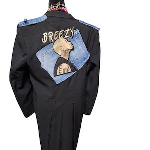 May include: Black blazer with denim shoulder accents and a denim patch on the back. The patch features an illustration of a person and the word "BREEZY" in gold lettering. The blazer is displayed on a mannequin.
