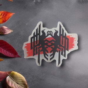 May include: A clear sticker featuring a black and red graphic design. The design includes two bird-like figures and geometric shapes, set against a red brushstroke. The sticker has a unique, irregular shape and is placed on a gray surface with colorful autumn leaves.