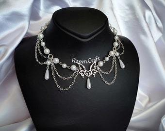 May include: A silver chain necklace with a butterfly pendant and white pearl accents. The necklace has a delicate, feminine design and is perfect for adding a touch of elegance to any outfit.
