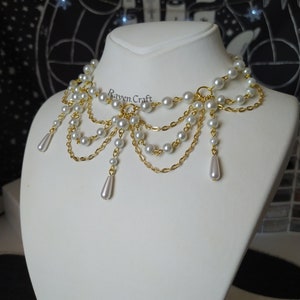 May include: A gold-toned necklace with multiple strands of faux pearls and delicate chains. The necklace features a cascading design with teardrop-shaped pearl pendants. The Raven.Craft logo is visible on the necklace.