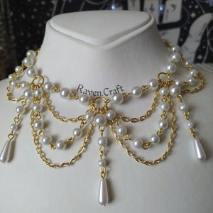 May include: A pearl and gold-tone necklace with the text "Raven Craft". The necklace features multiple strands of faux pearls and gold-colored chain, with teardrop-shaped pearl pendants.