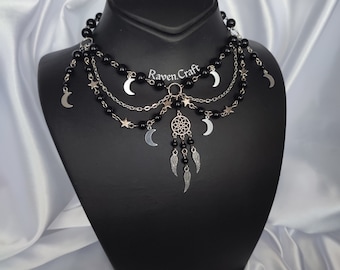 May include: A layered black beaded choker necklace with silver crescent moons, stars, and a dreamcatcher pendant. The necklace is displayed on a black mannequin bust.