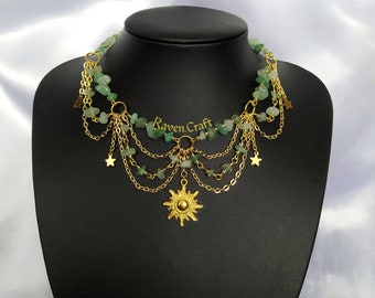 May include: A gold chain necklace with green gemstone beads and star charms. The necklace has a large sun pendant at the bottom. The text "Raven.Craft" is visible on the necklace.