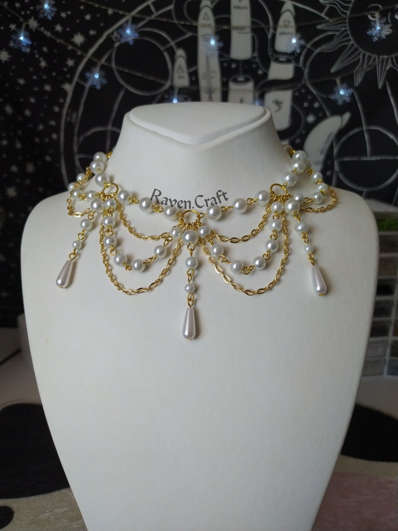 May include: A gold-toned choker necklace with multiple strands of faux pearls and delicate chains. The necklace features a cascading design with teardrop-shaped pearl pendants. The text "Raven.Craft" is visible on the image.