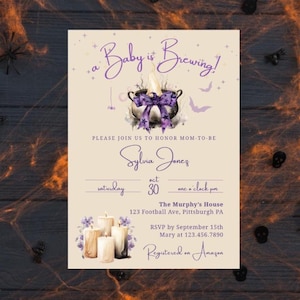 Pode incluir: Um convite para chá de bebê com tema de Halloween com o texto "a Baby is Brewing!" em escrita roxa. O design inclui um caldeirão, morcegos e detalhes florais. Detalhes: nome, data, hora e local.