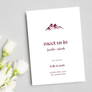 May include: Save the date card with a mountain range illustration in maroon. The text reads "meet us in boulder, colorado" and "save the date kelly & matt october 8th, 2016 the smokey bear"