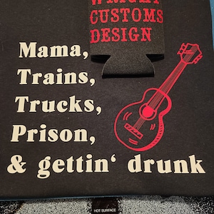 Può includere: Maglietta nera con testo bianco che recita "Mama, Trains, Trucks, Prison, & gettin' drunk". Un grafico di chitarra rosso è sul lato destro della maglietta. Un refrigeratore di lattine nero con testo rosso che recita "WRIGHT CUSTOMS DESIGN" è sul lato sinistro della maglietta.