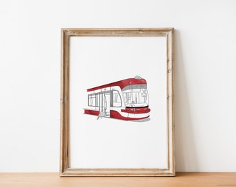 Puede incluir: Impresión artística enmarcada que presenta una ilustración de tranvía rojo y blanco. La obra de arte es un dibujo lineal detallado con acentos rojos, sobre un fondo blanco. La impresión se muestra en un marco de madera.