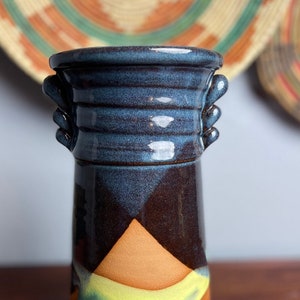 May include: A ceramic vase with a blue, brown, and orange glaze. The vase has two handles on the sides and a flared opening.