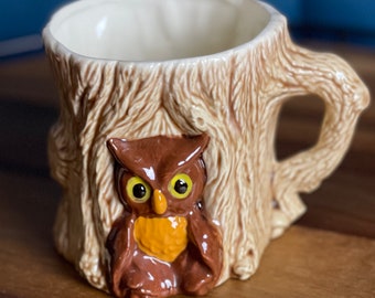 May include: A ceramic mug shaped like a tree stump with a brown owl perched on the front. The mug has a white interior and a brown handle.