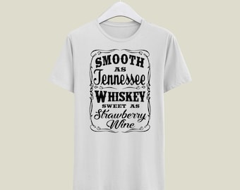 Op de afbeelding: Wit t-shirt met een zwarte opdruk met de tekst "Smooth as Tennessee Whiskey, Sweet as Strawberry Wine". De tekst is in een decoratief lettertype. Het t-shirt hangt aan een witte hanger.