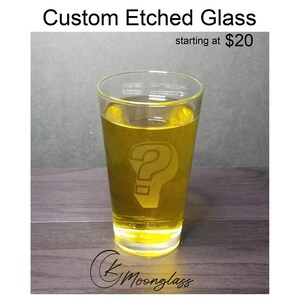 May include: A clear glass with a question mark etched into the side. The glass is filled with a yellow liquid. The text "Custom Etched Glass starting at $20" is visible above the glass.