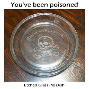 May include: Clear glass pie dish with etched skull and crossbones design. The text "You've been poisoned" is etched around the rim. The words "Etched Glass Pie Dish" are at the bottom.