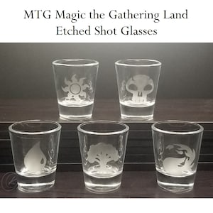 May include: Six clear glass shot glasses with etched Magic: The Gathering land symbols. The symbols are a sun, a skull, a teardrop, a tree, and a flame.