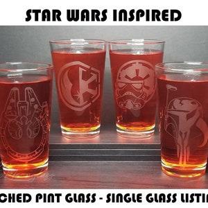 May include: Four etched pint glasses with Star Wars inspired designs. The glasses are filled with a red liquid and are arranged on a wooden surface. The designs include a TIE fighter, a Stormtrooper helmet, the Rebel Alliance symbol, and a Mandalorian helmet.