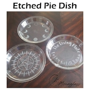 May include: Three glass pie dishes with etched designs. The first dish has a crescent moon design, the second has a pentagram with the words "GRAM", "MA", "TE", "NOL" around it, and the third has the words "The Giving Plate Enjoy Refill Papa" around the edge.