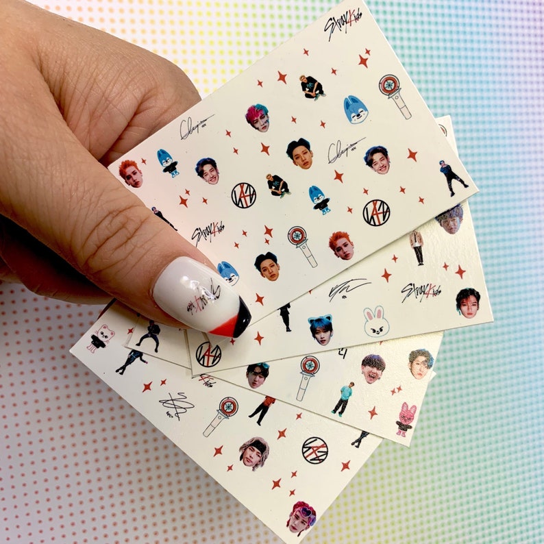 Op de afbeelding: Set van vijf vellen witte nagelstickers met afbeeldingen van een K-pop boyband, waaronder de gezichten van de bandleden, een microfoon, een ster en de bandnaam "Stray Kids".