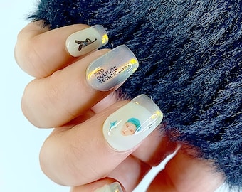 May include: Close-up of a hand with several white nail stickers. The stickers feature a cartoon character, the text "NEO CULTURE TECHNOLOGY", and a graphic of a star.