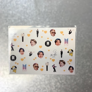 May include: A sheet of stickers featuring images of a musical group. The stickers include portraits, logos, and signatures, along with yellow heart and light stick graphics. The stickers are on a white background.