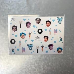 May include: A sheet of stickers featuring images of people, hearts, and logos. The stickers have a white background with blue hearts scattered throughout. The images include faces, logos, and figures in various poses. The stickers are in a clear plastic sleeve.