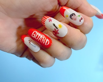 May include: Close-up of a hand with red and white nail art. The nails are decorated with flowers, a person's face, and the word "GUARD".