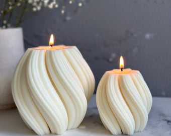 May include: Two white, swirl-shaped candles with a flame on top of each. The candles are on a white surface.